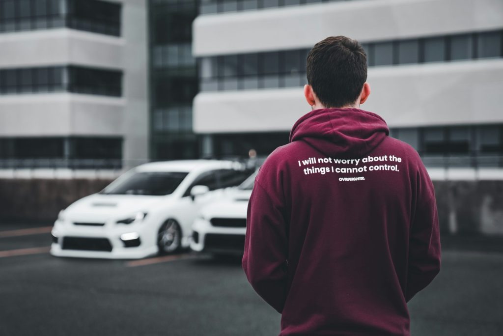 a man in a maroon hoodie standing in front of a white car