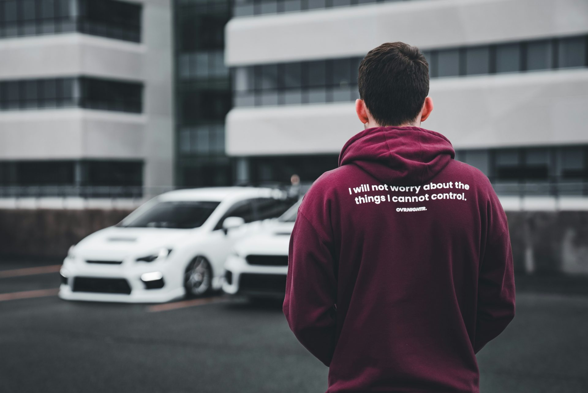 a man in a maroon hoodie standing in front of a white car